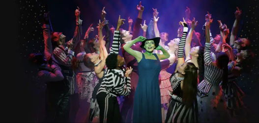 Wicked comédie musicale. acteurs sur la scène. Au moment même ou Wicked sort dans les salles de cinémas Françaises, Wicked, la comédie musicale bat sont plein depuis des années au Gershwin Theater. Plongez vous dans cette étonnante histoire dont les américains raffolent, autant par l’ambiance mystique que sa mise en scène remarquable, au cœur du poumon artistique de Broadway. Odyssée Américaine