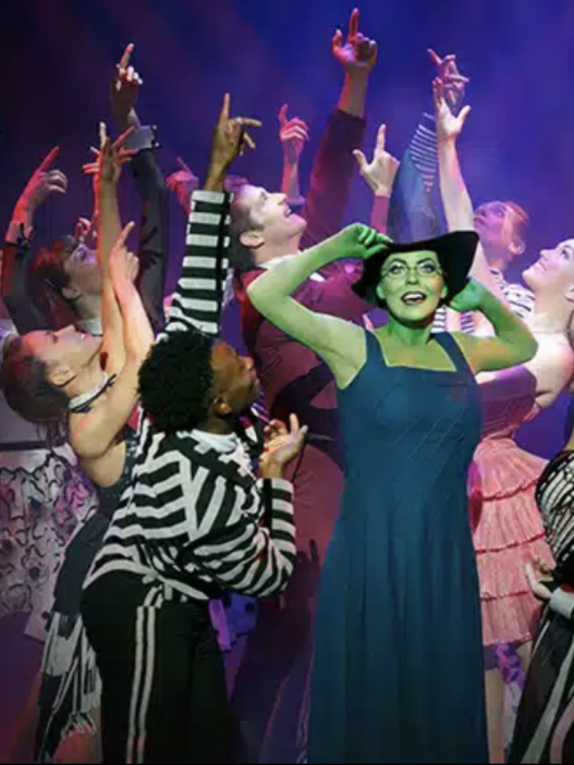 Wicked comédie musicale. acteurs sur la scène. Au moment même ou Wicked sort dans les salles de cinémas Françaises, Wicked, la comédie musicale bat sont plein depuis des années au Gershwin Theater. Plongez vous dans cette étonnante histoire dont les américains raffolent, autant par l’ambiance mystique que sa mise en scène remarquable, au cœur du poumon artistique de Broadway. Odyssée Américaine